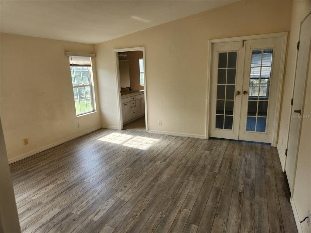 A bedroom with light-colored walls, wood-look flooring, a bathroom doorway, and French doors — 5165 TOPEKA AVENUE, ST CLOUD, FL
