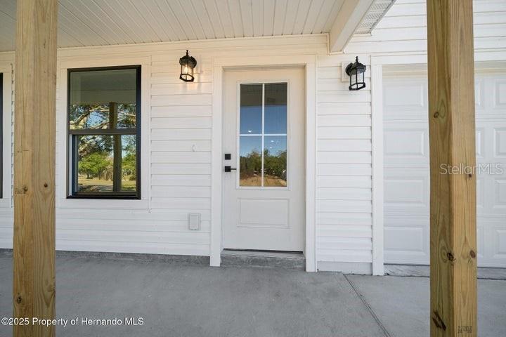 A white front door with a glass pane sits between two wooden porch posts — 6356 MARINER BOULEVARD, SPRING HILL, FL