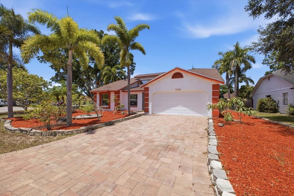 A single-story house with a paved driveway, palm trees, and red mulch landscaping — 720 50TH STREET E, BRADENTON, FL