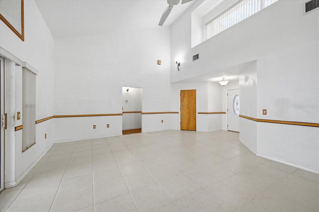 An empty, high-ceilinged room features white walls, tile flooring, and a wooden chair rail — 720 50TH STREET E, BRADENTON, FL
