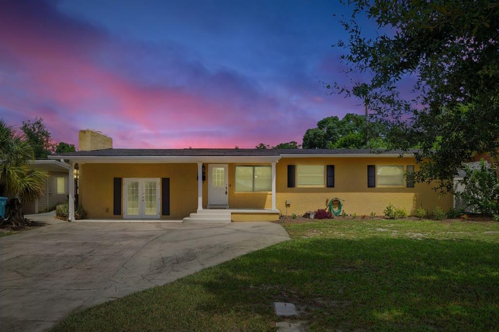 A single-story yellow house with a concrete driveway and a sunset sky in the background — 3707 PELICAN LANE, ORLANDO, FL