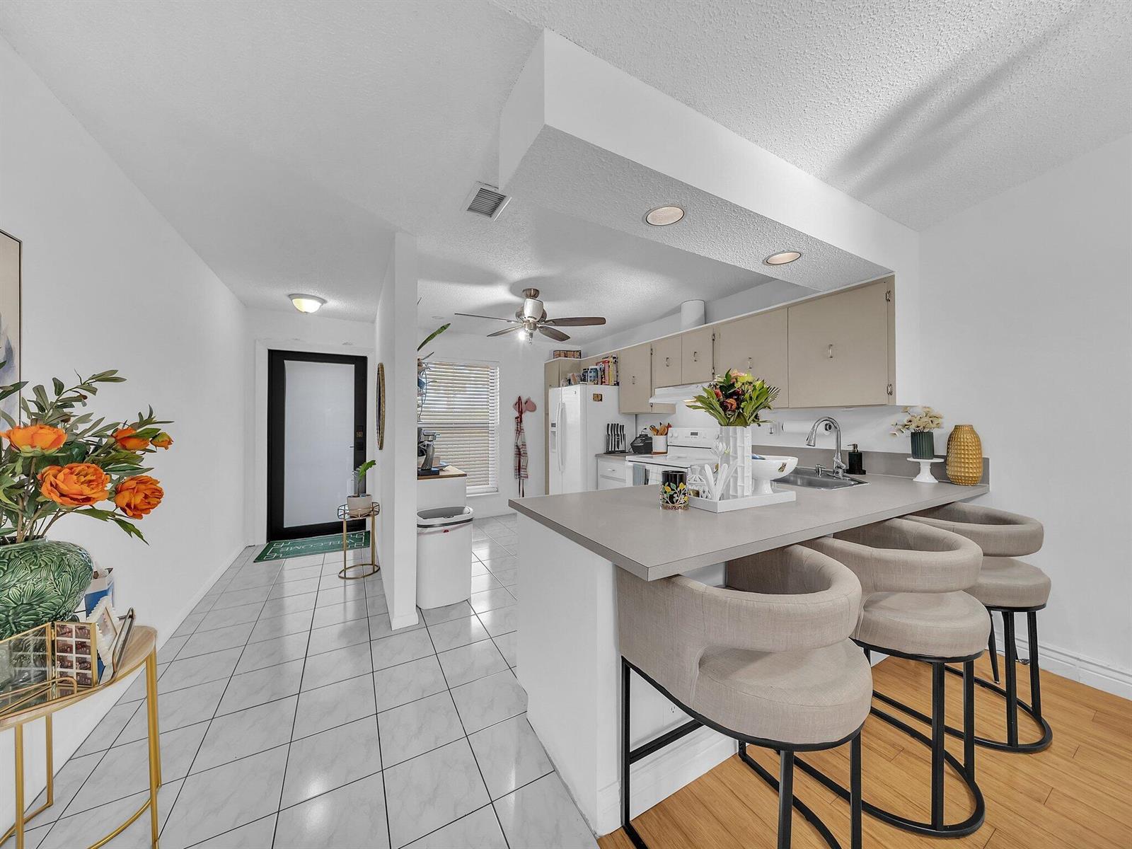 A kitchen with a breakfast bar, light-colored cabinets, and tile flooring next to an entryway — 1023 Banks Road # 201, Margate FL 33063, MARGATE, FL