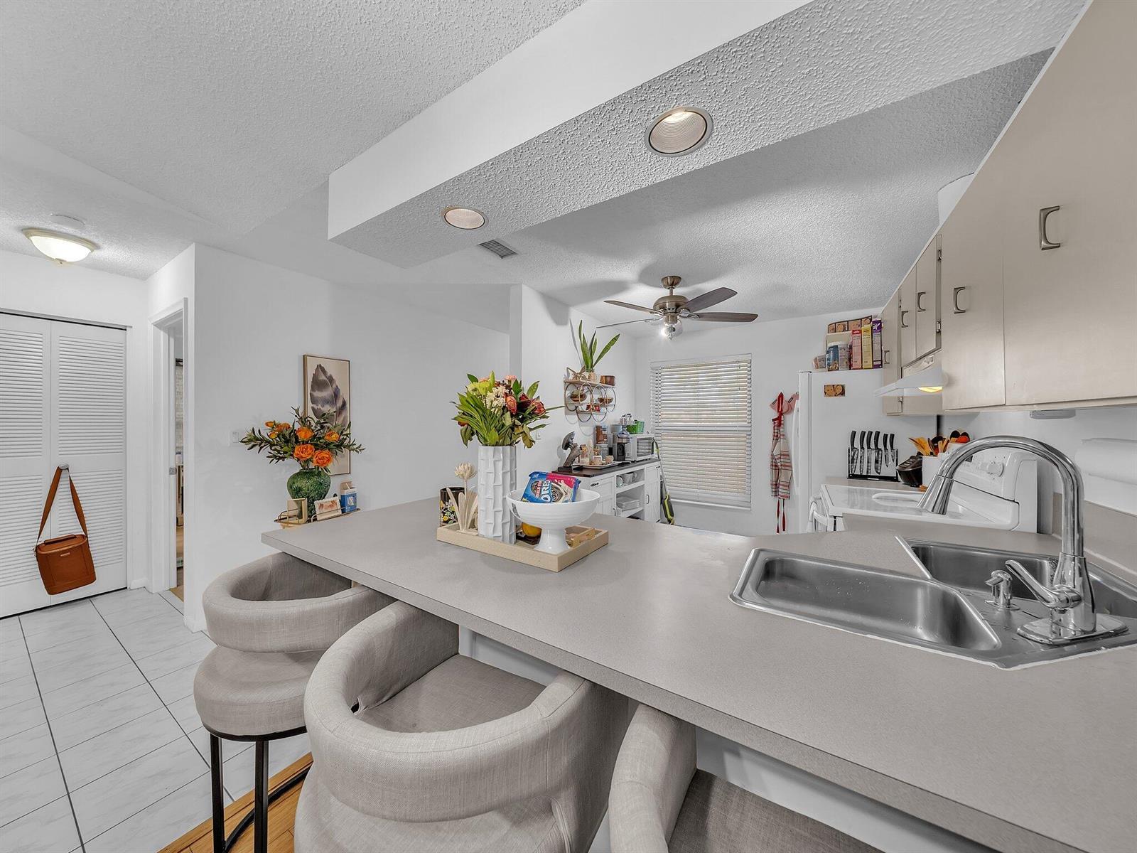 A kitchen features a gray countertop, a double sink, and three upholstered bar stools — 1023 Banks Road # 201, Margate FL 33063, MARGATE, FL