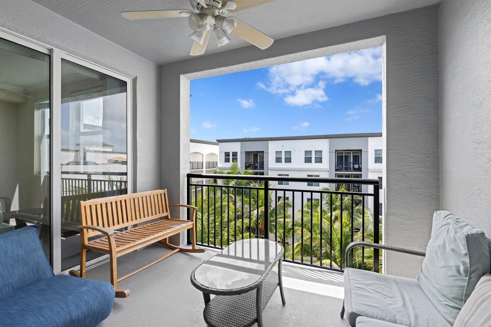 A balcony features a wooden rocking bench, a glass-topped table, and a view of palm trees — 1660 Renaissance Commons Boulevard # 2629, Boynton Beach FL 33426, BOYNTON BEACH, FL