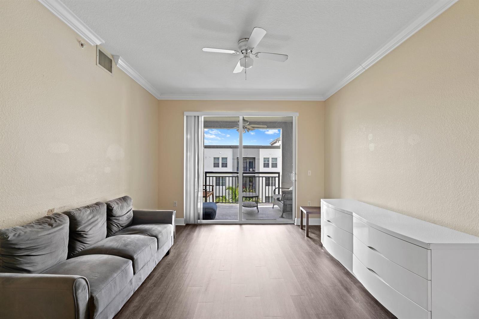A living room with a gray sofa, white dresser, ceiling fan, and sliding glass balcony doors — 1660 Renaissance Commons Boulevard # 2629, Boynton Beach FL 33426, BOYNTON BEACH, FL