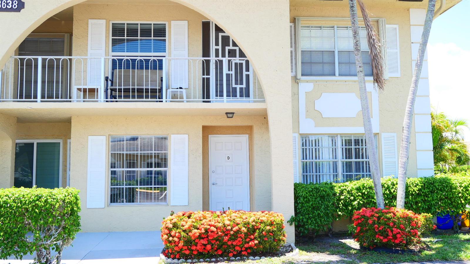 The exterior of a two-story tan stucco building features a balcony and a front door — 13638 Via Flora # D, Delray Beach FL 33484, DELRAY BEACH, FL