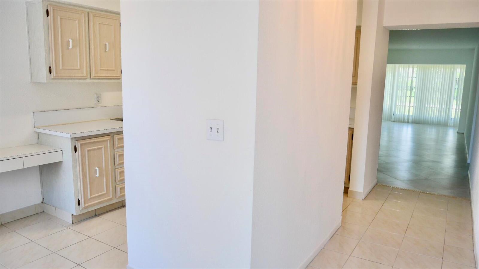 A kitchen with light wood cabinets and tile flooring leads to a bright living area — 13638 Via Flora # D, Delray Beach FL 33484, DELRAY BEACH, FL