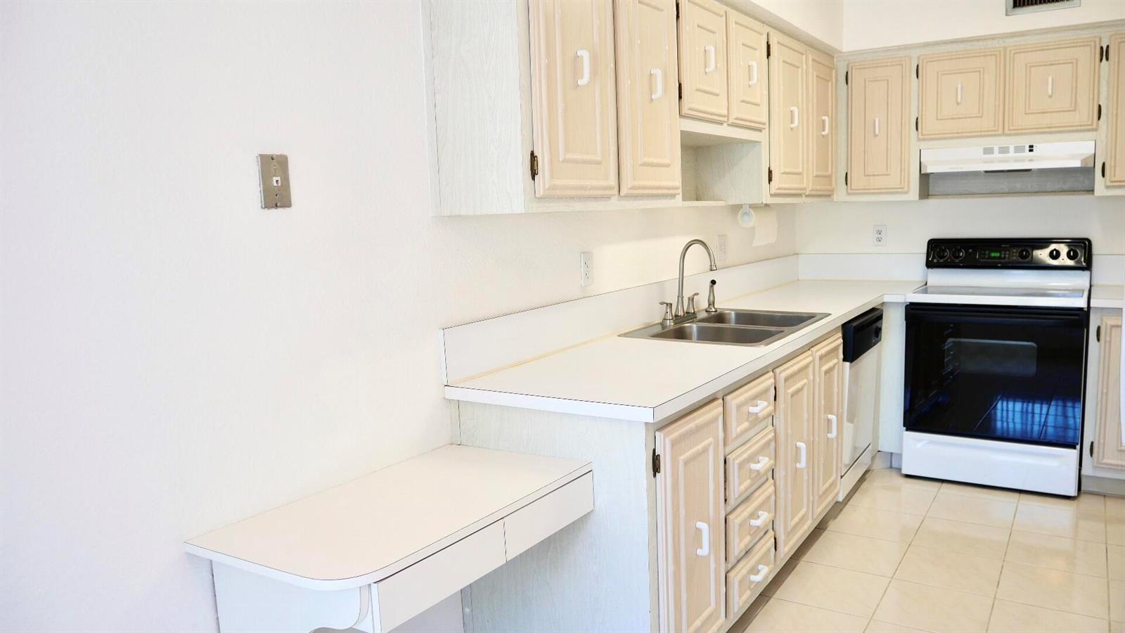 A kitchen features light-colored wooden cabinets, white countertops, a double sink, and a white stove — 13638 Via Flora # D, Delray Beach FL 33484, DELRAY BEACH, FL