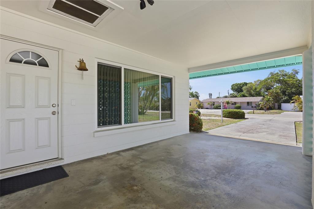 A covered concrete porch features a white front door, a large window, and a bell — 2101 JO AN DRIVE, SARASOTA, FL
