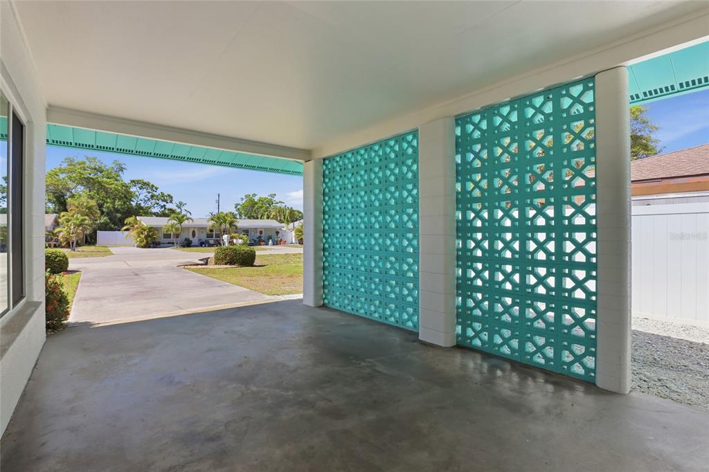 A covered carport features a concrete floor and decorative teal breeze block privacy walls — 2101 JO AN DRIVE, SARASOTA, FL