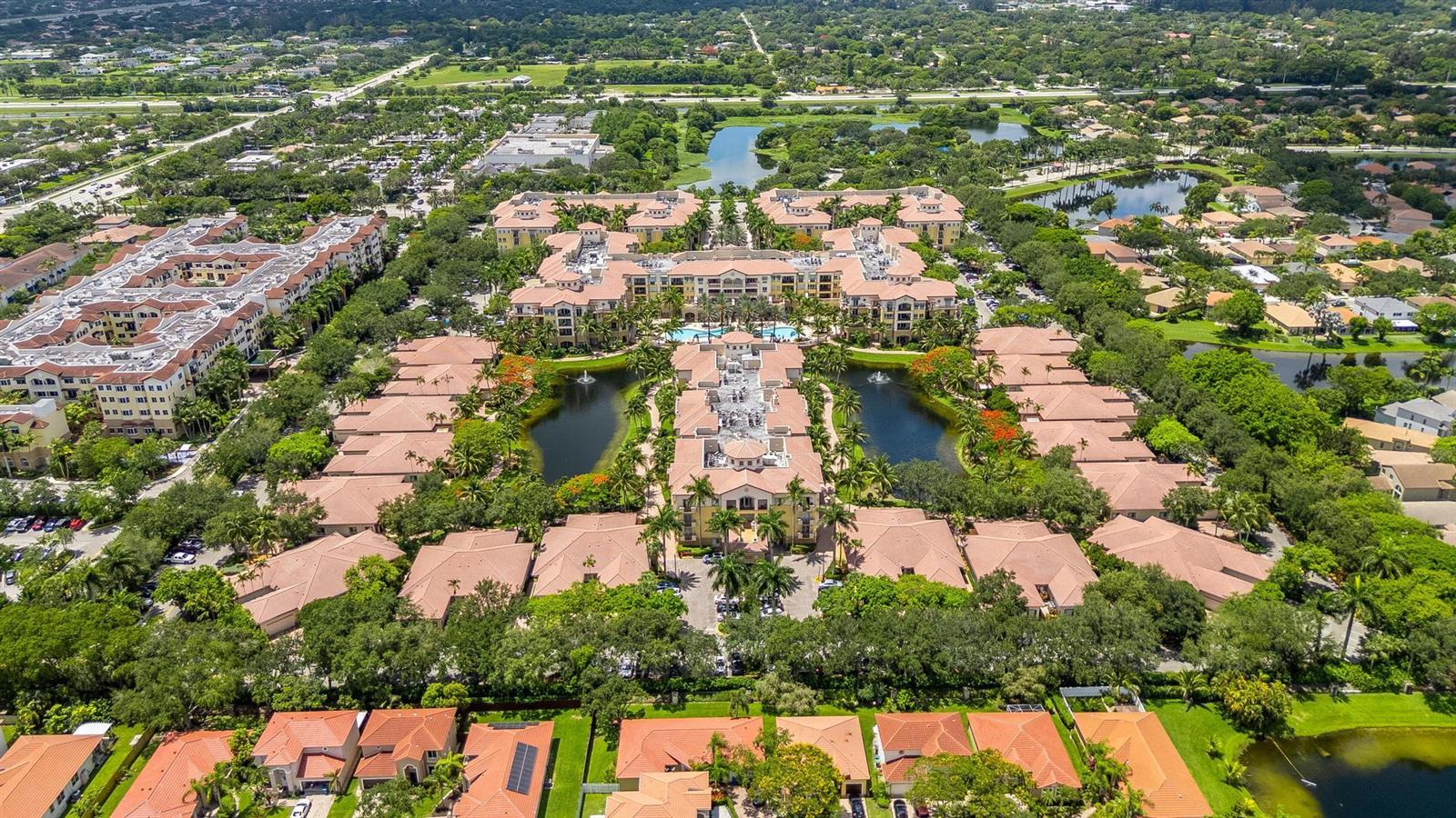 An aerial view of a large residential apartment complex with surrounding ponds and lush landscaping — 16102 Emerald Estates Drive # 128, Weston FL 33331, WESTON, FL