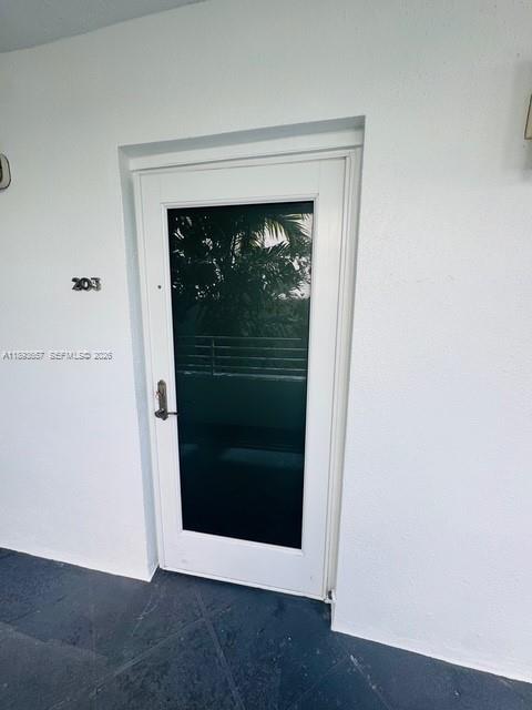 A white door with a dark glass panel is labeled with the number 203 — 7800 Collins Ave # 203, Miami Beach FL 33141, MIAMI BEACH, FL