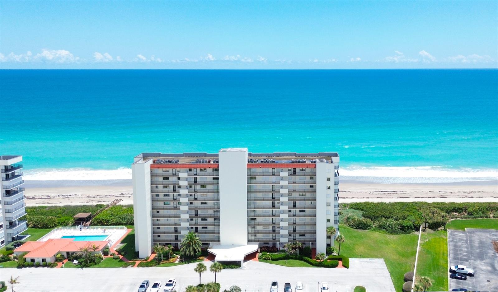 An aerial view of a beachfront condominium building with a pool and parking lot — 9490 S Ocean Drive Apt 710, Jensen Beach FL 34957, JENSEN BEACH, FL