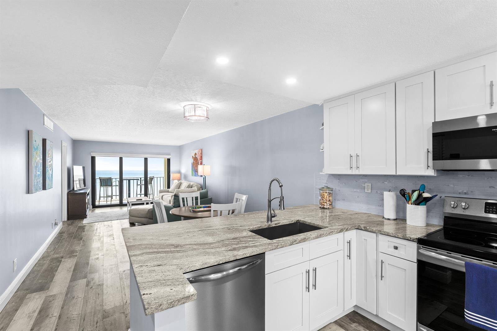 A kitchen with white cabinets and granite countertops overlooks a living area with ocean views — 9490 S Ocean Drive Apt 710, Jensen Beach FL 34957, JENSEN BEACH, FL