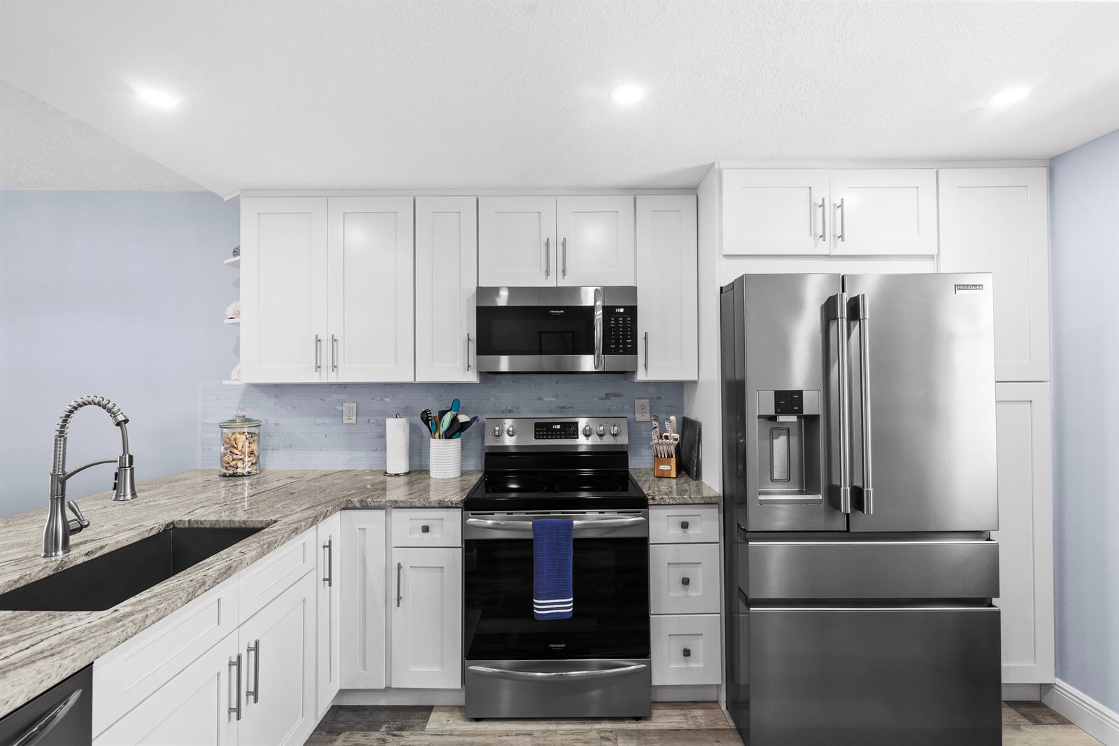 A kitchen features white cabinets, granite countertops, stainless steel appliances, and a light blue backsplash — 9490 S Ocean Drive Apt 710, Jensen Beach FL 34957, JENSEN BEACH, FL