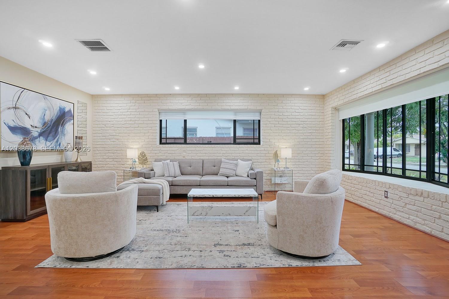 A living room features a white brick wall, hardwood floors, and a gray sofa set — 850 NE 182nd Ter, North Miami Beach FL 33162, NORTH MIAMI BEACH, FL