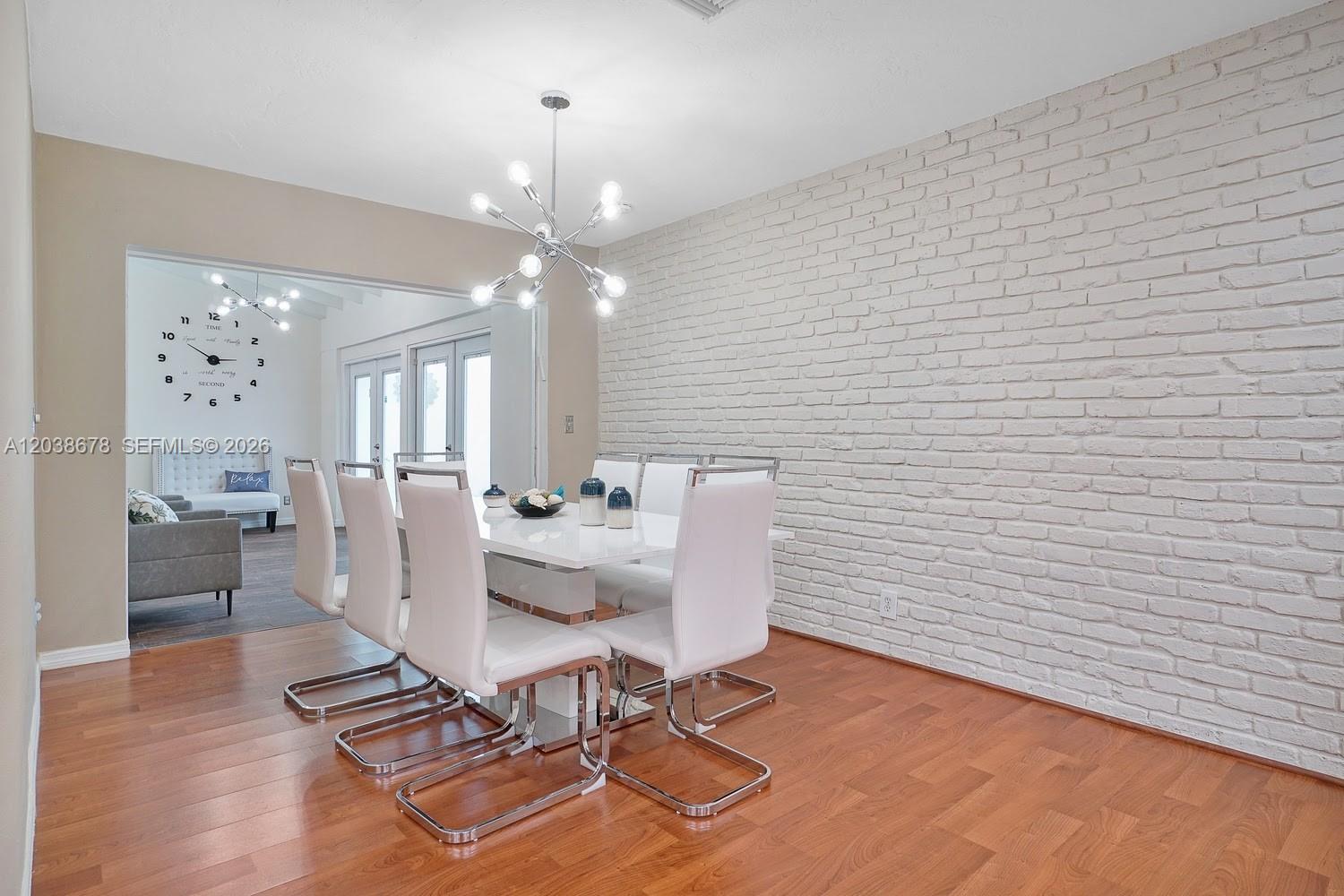 A dining room features a white table, six chairs, a modern chandelier, and a brick wall — 850 NE 182nd Ter, North Miami Beach FL 33162, NORTH MIAMI BEACH, FL