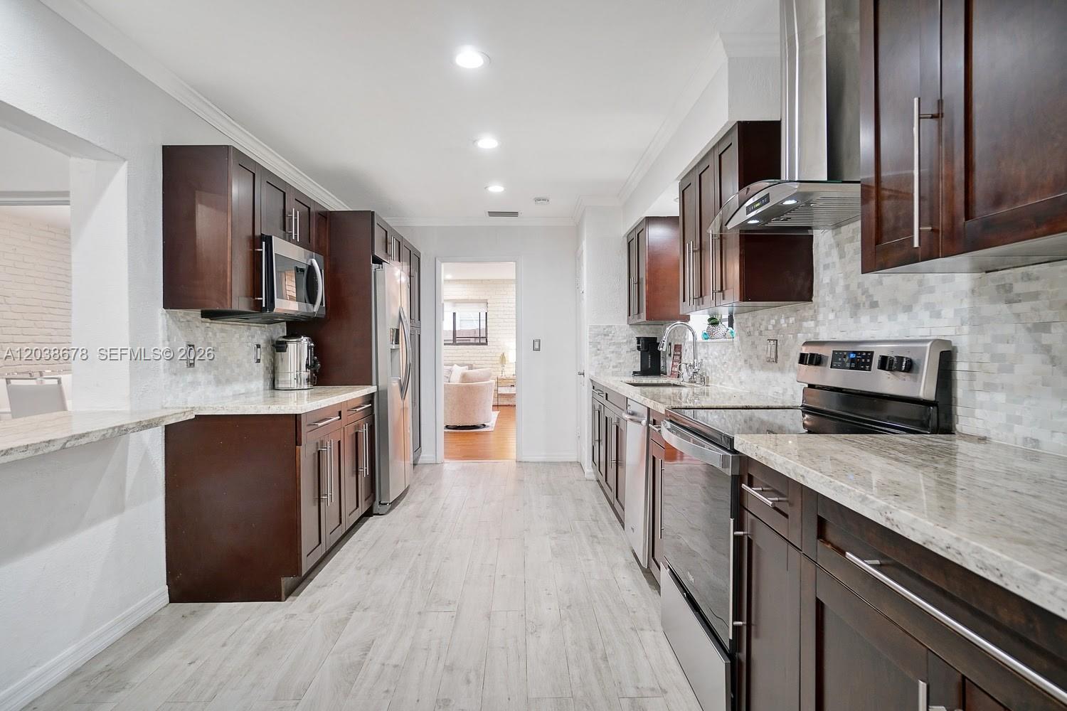 A galley kitchen features dark wood cabinets, granite countertops, stainless steel appliances, and light flooring — 850 NE 182nd Ter, North Miami Beach FL 33162, NORTH MIAMI BEACH, FL