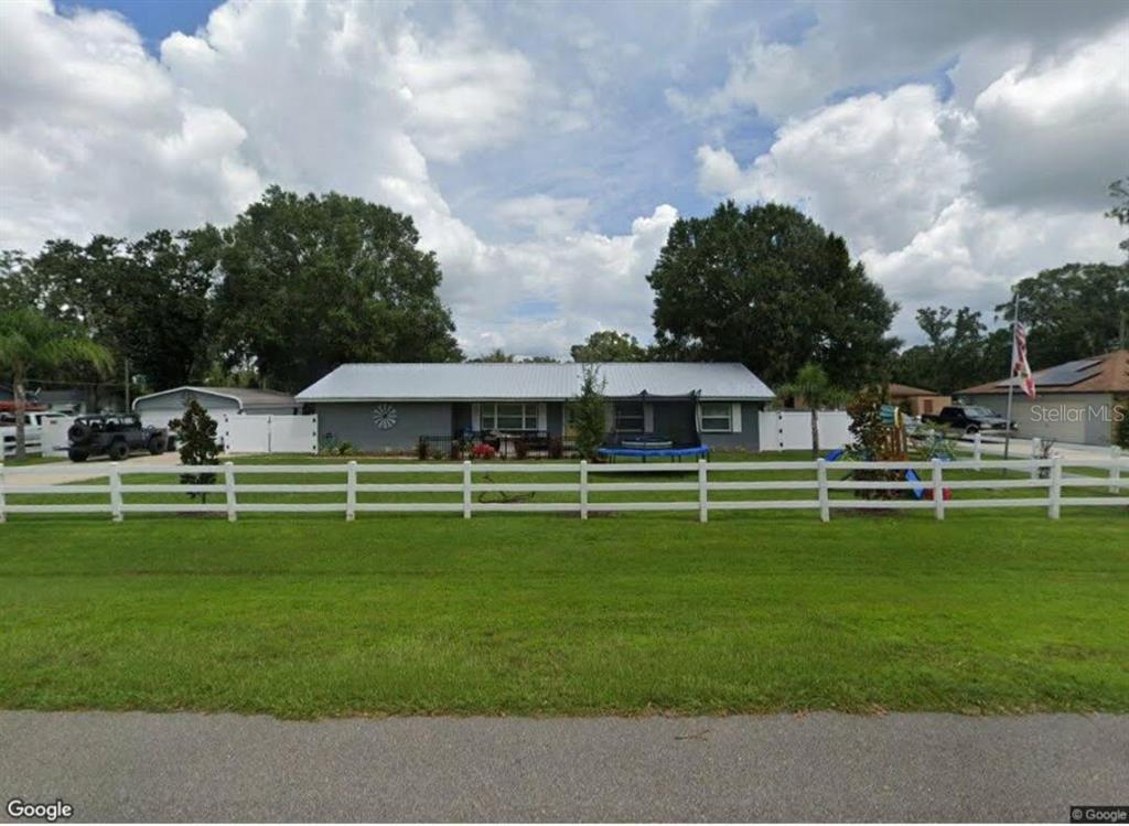 A gray single-story house with a metal roof, attached garage, and a large grassy yard — 3455 TANAGER LANE W, MULBERRY, FL