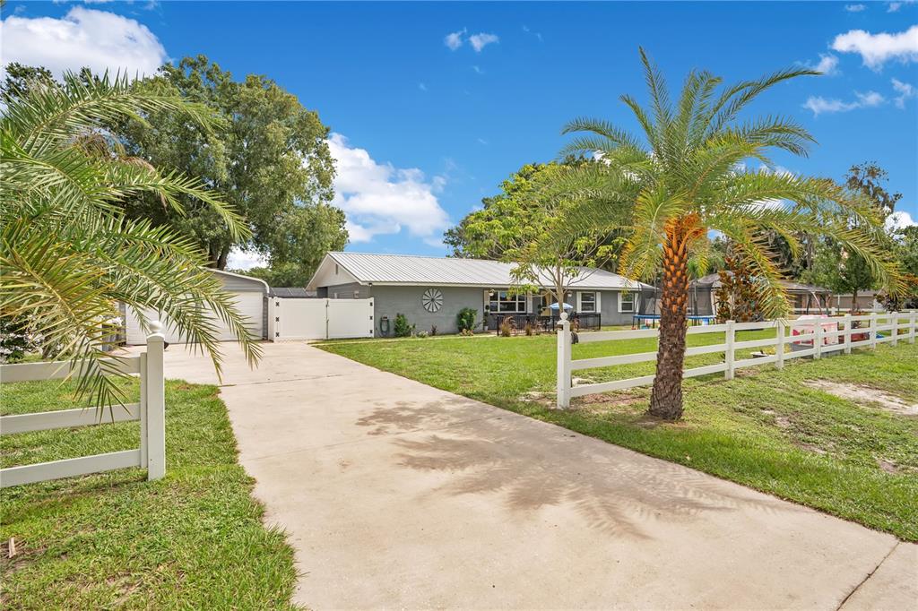 A single-story gray house with a metal roof, concrete driveway, and white vinyl fencing — 3455 TANAGER LANE W, MULBERRY, FL
