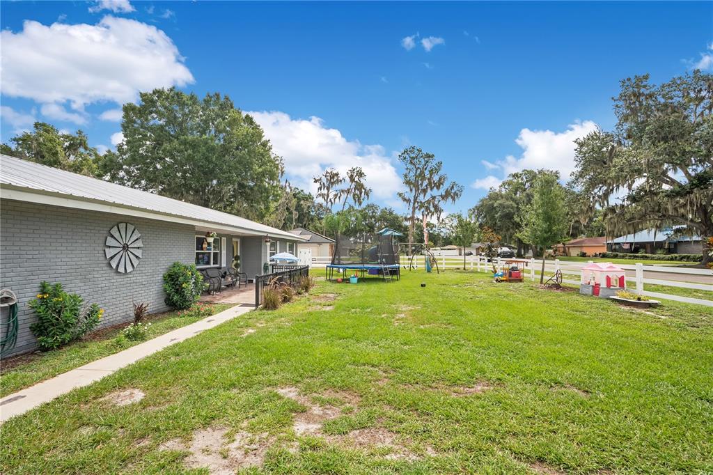 A gray brick house with a metal roof overlooks a grassy backyard with a trampoline — 3455 TANAGER LANE W, MULBERRY, FL