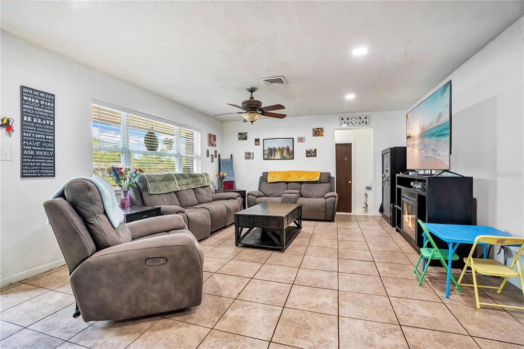 A living room features tile flooring, grey reclining furniture, a television, and a child's table — 3455 TANAGER LANE W, MULBERRY, FL