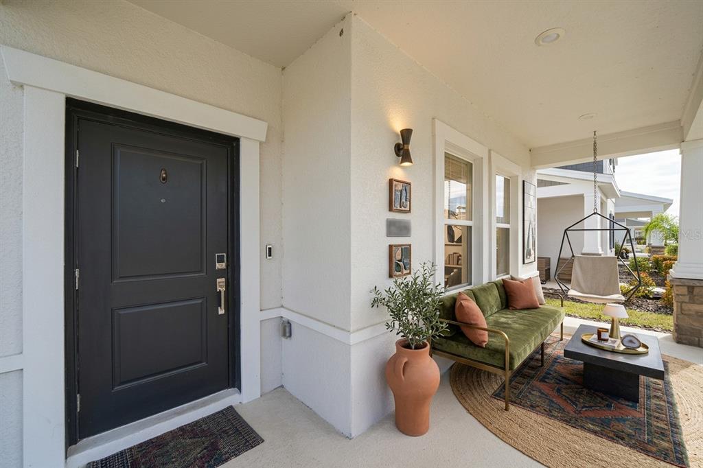A covered front porch features a dark door, green velvet sofa, and hanging chair — 6349 BLISSFUL STREET, CLERMONT, FL