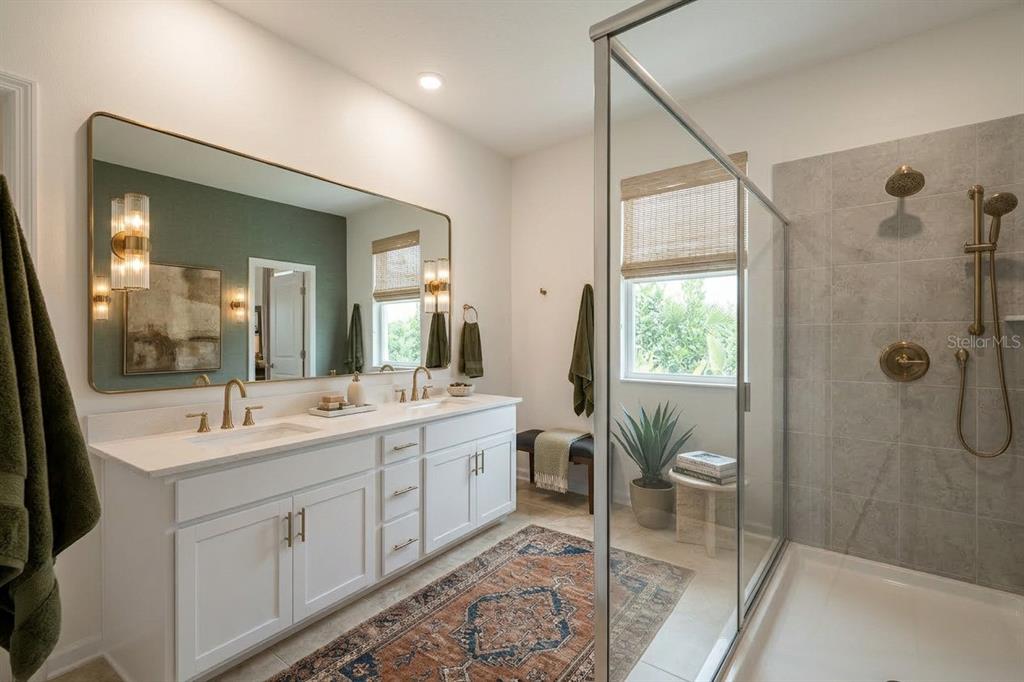 A bathroom features a double vanity with gold fixtures, a large mirror, and a glass shower — 6349 BLISSFUL STREET, CLERMONT, FL