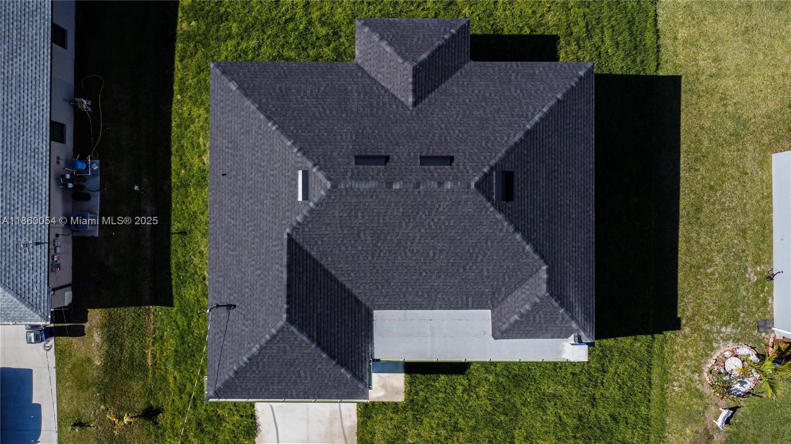 An aerial view shows the dark shingled roof of a house surrounded by green grass — 3610 SW 22ND ST, Lehigh Acres FL 33976, LEHIGH ACRES, FL