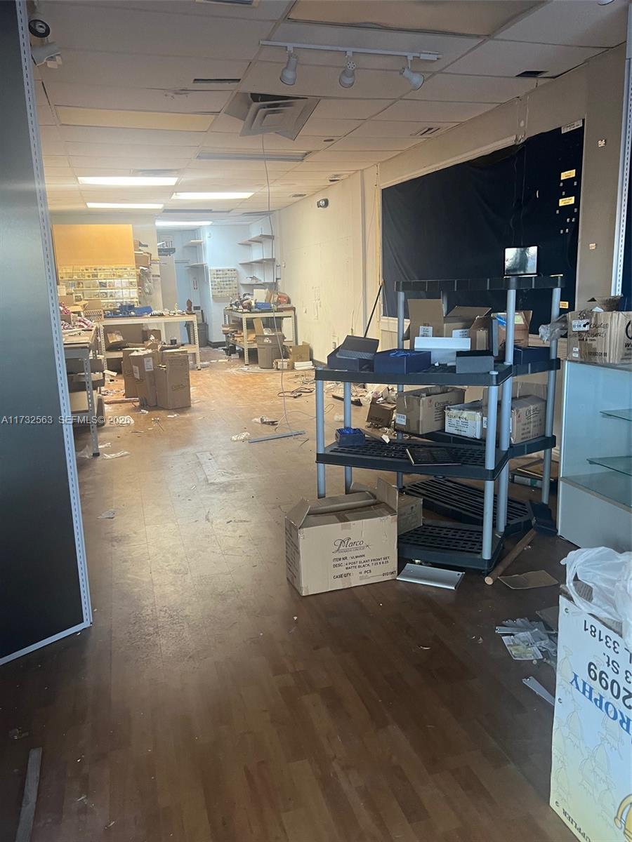A cluttered commercial space with wood-look flooring, drop ceilings, and metal shelving units — 1948 NE 123rd St # 105, North Miami FL 33181, NORTH MIAMI, FL