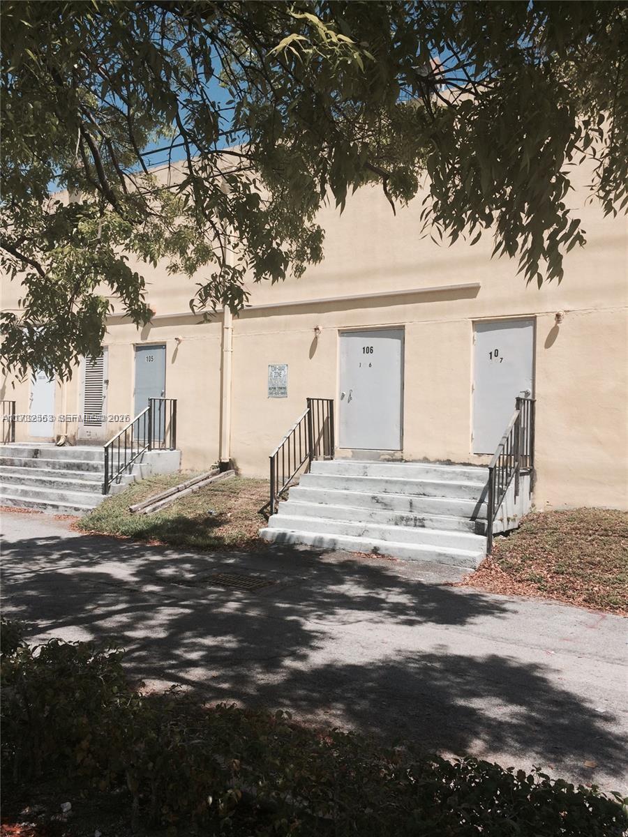 A row of industrial-style exterior doors with concrete stairs and metal railings under tree shade — 1948 NE 123rd St # 105, North Miami FL 33181, NORTH MIAMI, FL