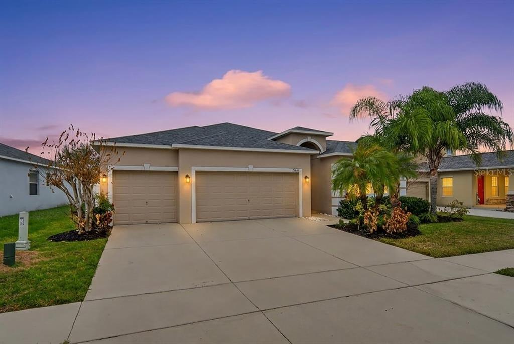 A tan single-story house features a three-car garage and a concrete driveway at dusk — 2854 YOUNGFORD STREET, ORLANDO, FL