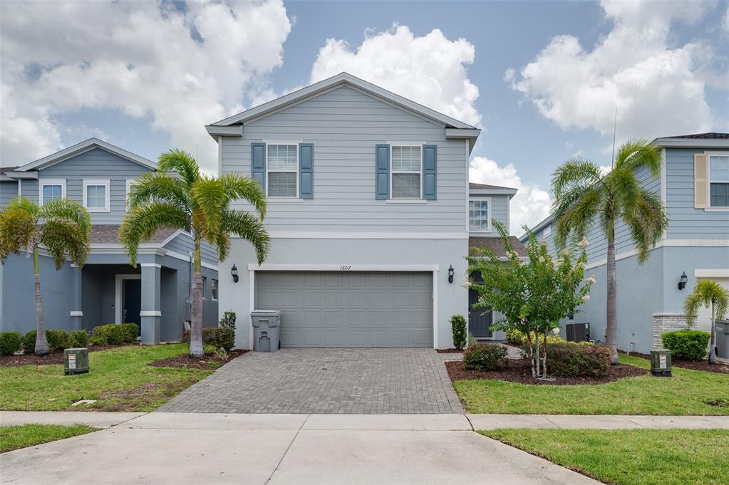 A two-story house with light blue siding, a gray garage door, and palm trees — 1607 KONA LANE, DAVENPORT, FL