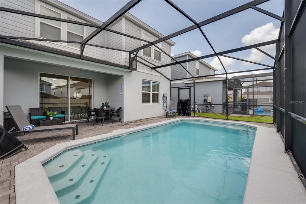 A screened-in patio features a rectangular swimming pool with steps and outdoor furniture — 1607 KONA LANE, DAVENPORT, FL