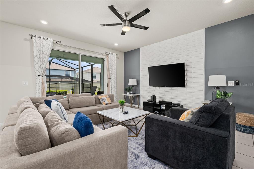 A living room features a white brick accent wall, a sectional sofa, and sliding glass doors — 1607 KONA LANE, DAVENPORT, FL