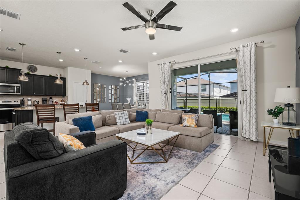 A living room with a sectional sofa, ceiling fan, and sliding doors opening to a pool — 1607 KONA LANE, DAVENPORT, FL
