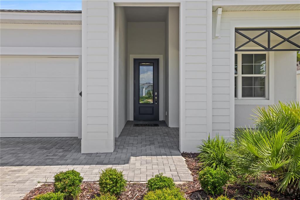 A white house exterior features a dark front door, a garage, and a paved walkway — 948 CLUB CRESSWIND DRIVE, LADY LAKE, FL