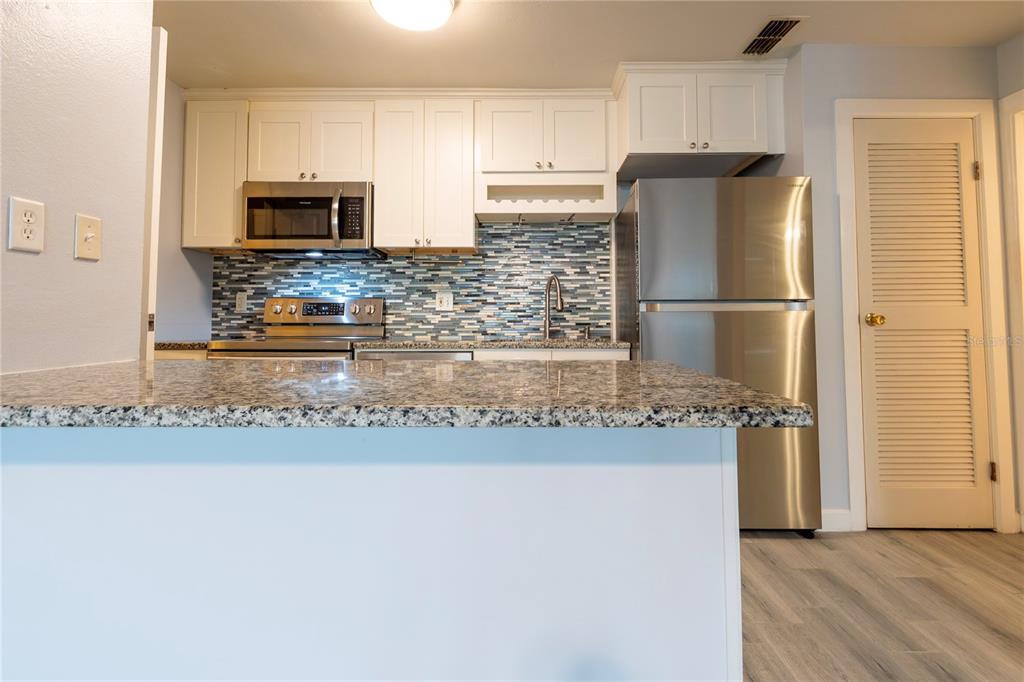 A kitchen features white cabinets, stainless steel appliances, a granite countertop, and a blue backsplash — 1400 GANDY BOULEVARD N UNIT 1010, ST PETERSBURG, FL