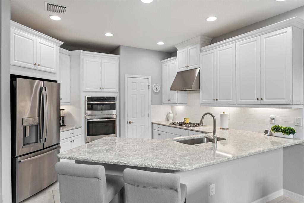 A modern kitchen features white cabinets, stainless steel appliances, and a granite-topped peninsula with seating — 8524 ARABELLA LANE, SEMINOLE, FL
