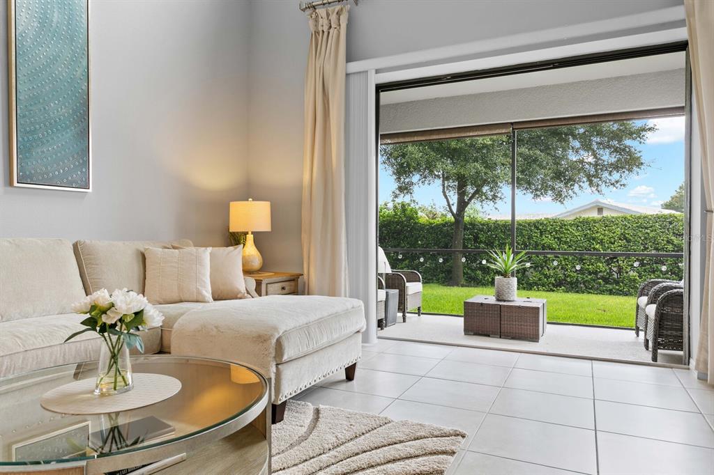 A living room with a beige sectional sofa opens to a screened-in patio with greenery — 8524 ARABELLA LANE, SEMINOLE, FL