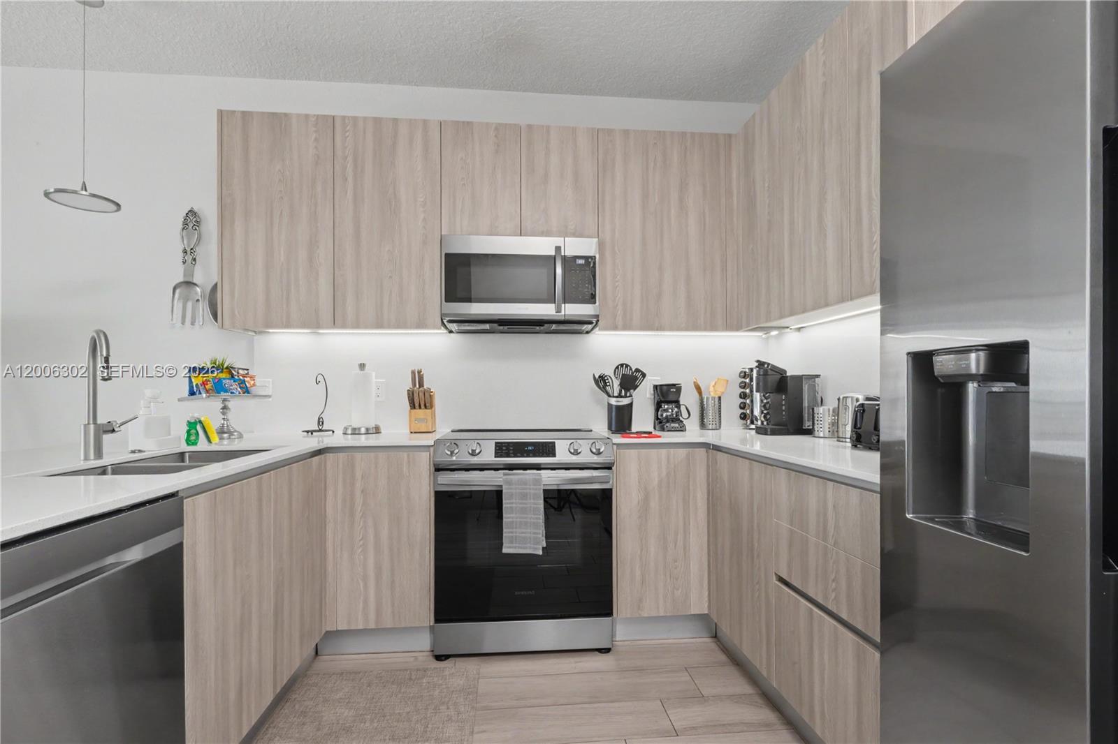 A modern kitchen features light wood-grain cabinets, stainless steel appliances, and white countertops — 17416 Hidden Forest # 0, Clermont FL 34714, CLERMONT, FL