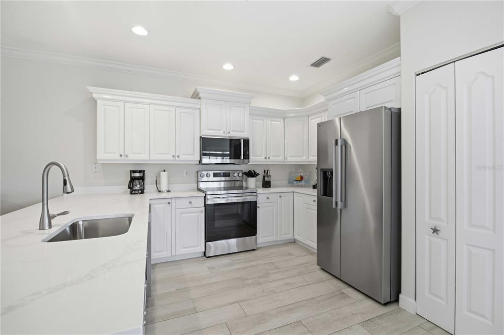 A modern kitchen features white cabinets, stainless steel appliances, and a white quartz countertop island — 215 81ST STREET, HOLMES BEACH, FL