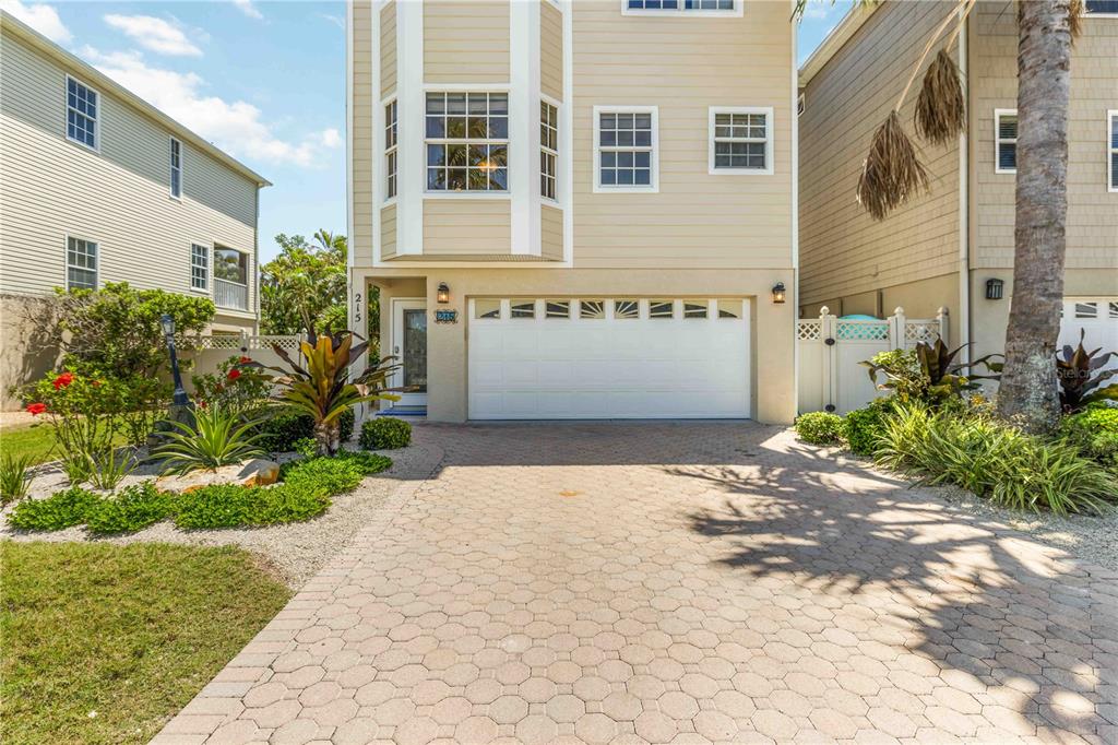 A three-story house with a beige exterior, a white garage door, and a paved driveway — 215 81ST STREET, HOLMES BEACH, FL