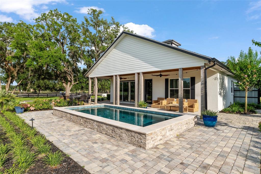 A backyard features a raised rectangular swimming pool on a stone patio beside a house — 11140 NW 160TH AVENUE, MORRISTON, FL