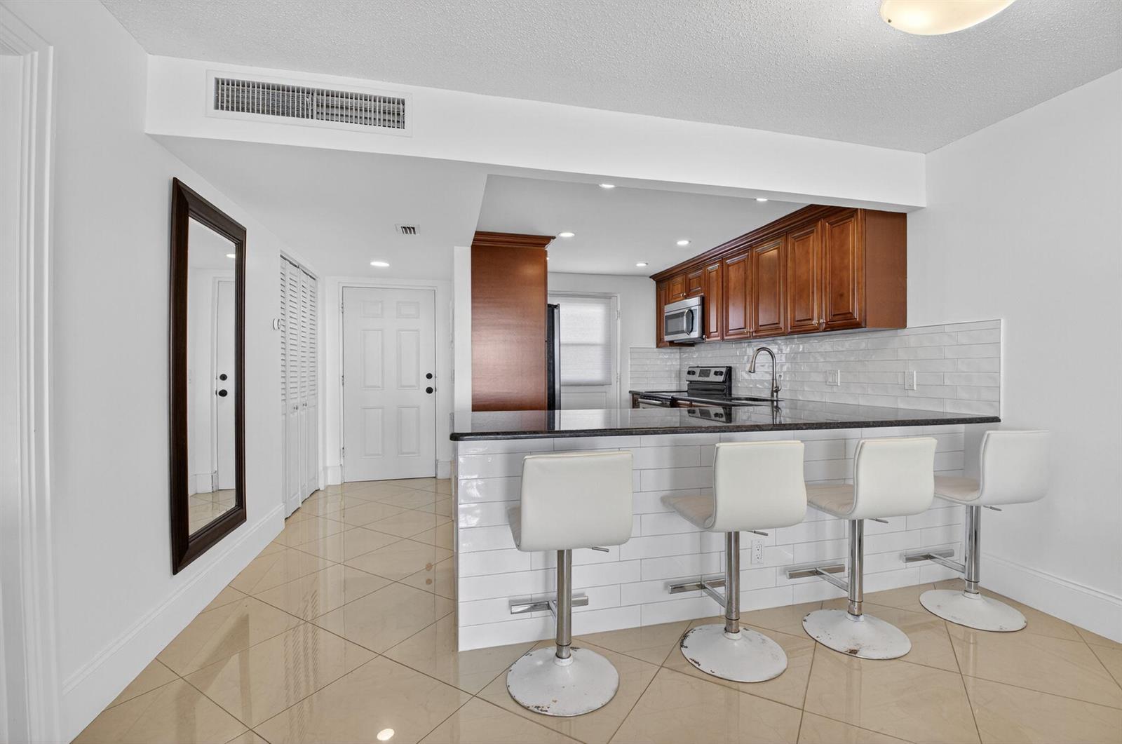 A kitchen features wood cabinets, a black countertop, and four white bar stools — 5500 NW 2nd Avenue # 718, Boca Raton FL 33487, BOCA RATON, FL