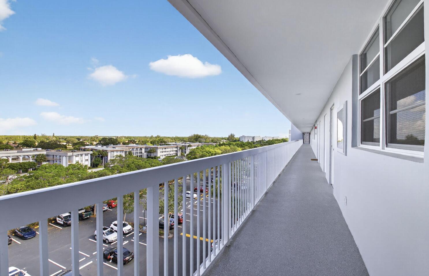 An outdoor apartment building walkway with a white railing overlooking a parking lot and trees — 5500 NW 2nd Avenue # 718, Boca Raton FL 33487, BOCA RATON, FL