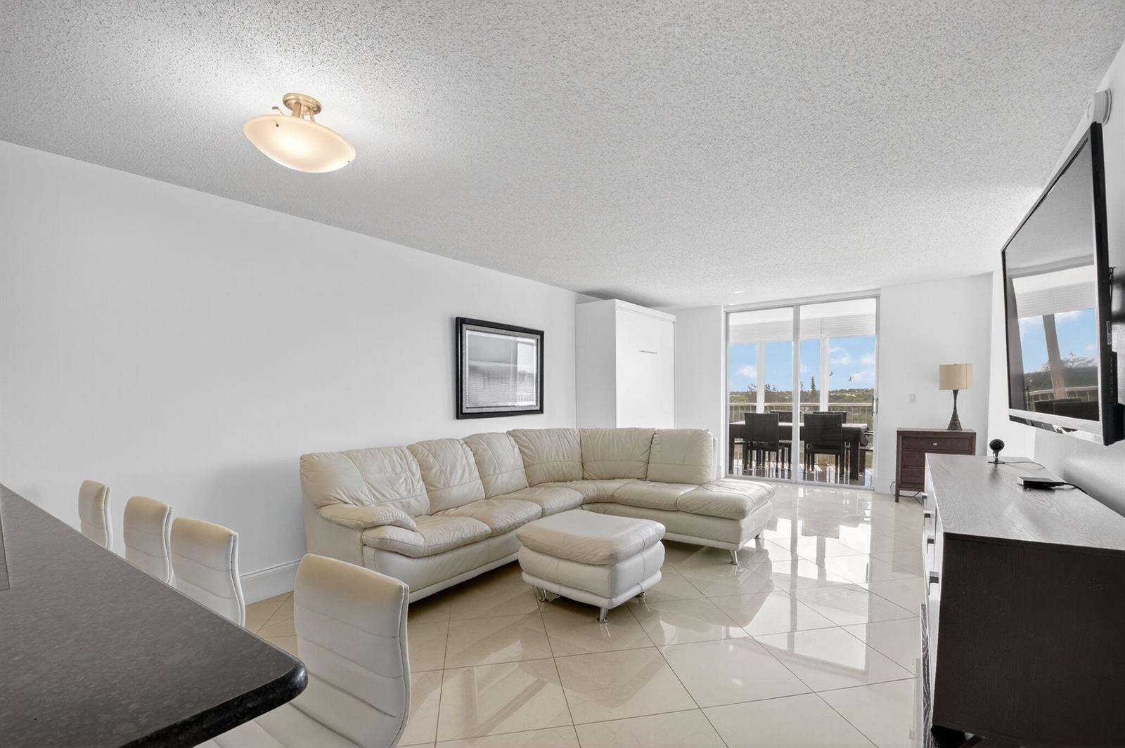 A living room with a white sectional sofa, tile flooring, and a sliding glass door — 5500 NW 2nd Avenue # 718, Boca Raton FL 33487, BOCA RATON, FL