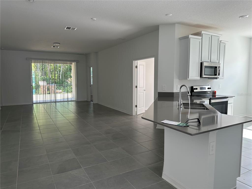 A kitchen with a gray island and white cabinets opens to a tiled living area — 4162 BABBLING BROOK WAY UNIT A, KISSIMMEE, FL