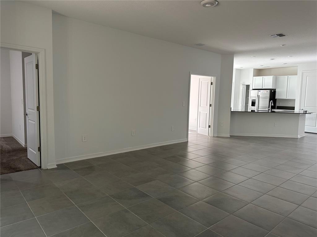 An open-concept living area features large gray floor tiles, white walls, and a kitchen view — 4162 BABBLING BROOK WAY UNIT A, KISSIMMEE, FL