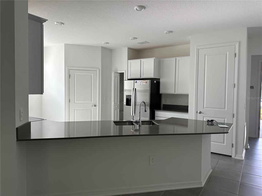 A kitchen features a dark countertop island, white cabinetry, stainless steel appliances, and tile flooring — 4162 BABBLING BROOK WAY UNIT A, KISSIMMEE, FL